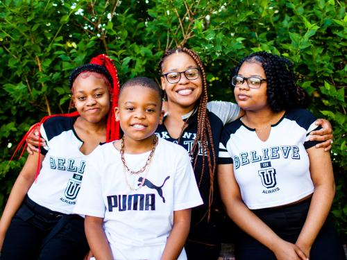 A young Black mother with 2 daughters and a son, in front of greenery.