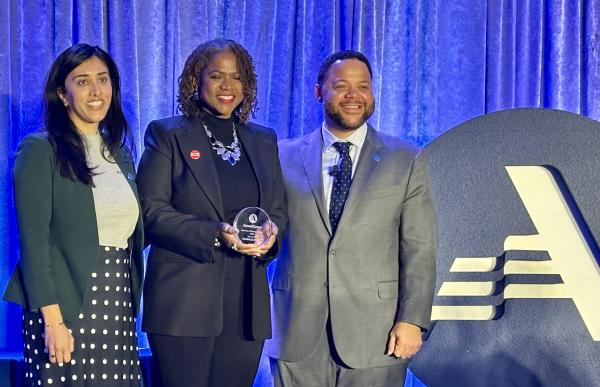 Three people stand in front of the AmeriCorp logo holding an award.