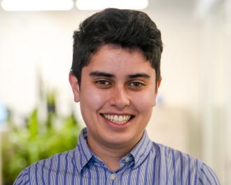 A person with dark hair and blue striped shirt smiles for the camera