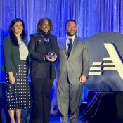 Three people stand in front of the AmeriCorp logo holding an award.