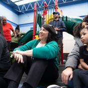 Woman sits on floor, smiling, next to families.