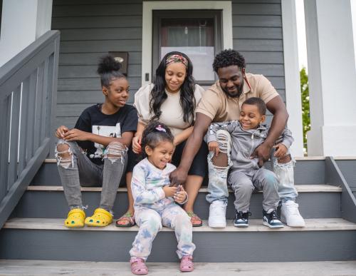 A mother and father sit on their porch with their three children.