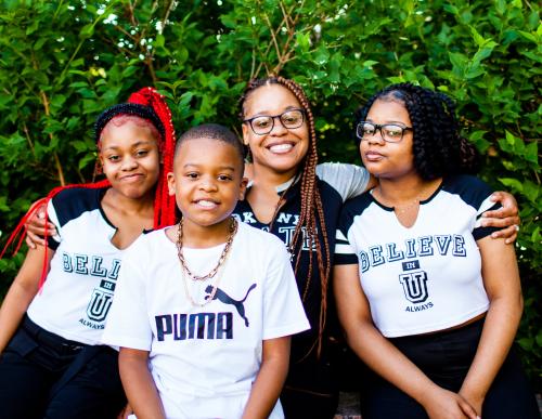 A young Black mother with 2 daughters and a son, in front of greenery.