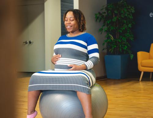 Expectant mother sits on exercise ball holding stomach.