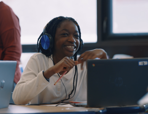 Young girl smiling, wearing headphones, sitting behind a computer