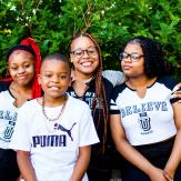 A young Black mother with 2 daughters and a son, in front of greenery.