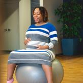 Expectant mother sits on exercise ball holding stomach.
