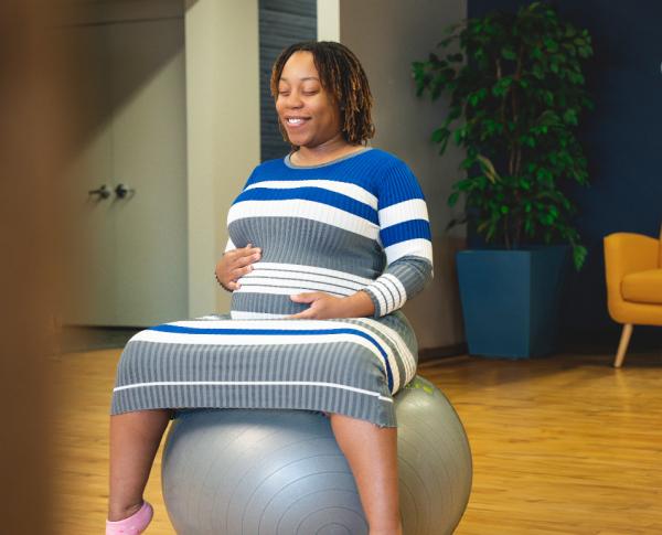 Expectant mother sits on exercise ball holding stomach.