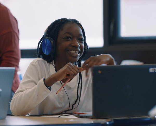 Young girl smiling, wearing headphones, sitting behind a computer