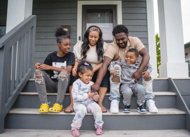 A mother and father sit on their porch with their three children.