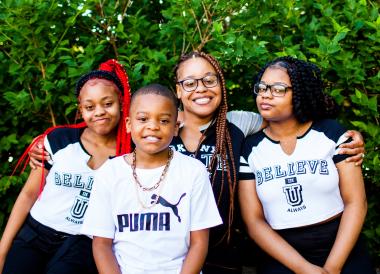 A young Black mother with 2 daughters and a son, in front of greenery.