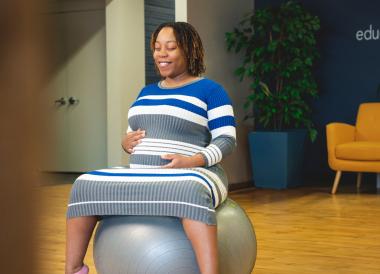 Expectant mother sits on exercise ball holding stomach.