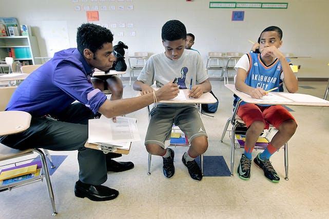 North Minneapolis teacher sits next to two students in desks