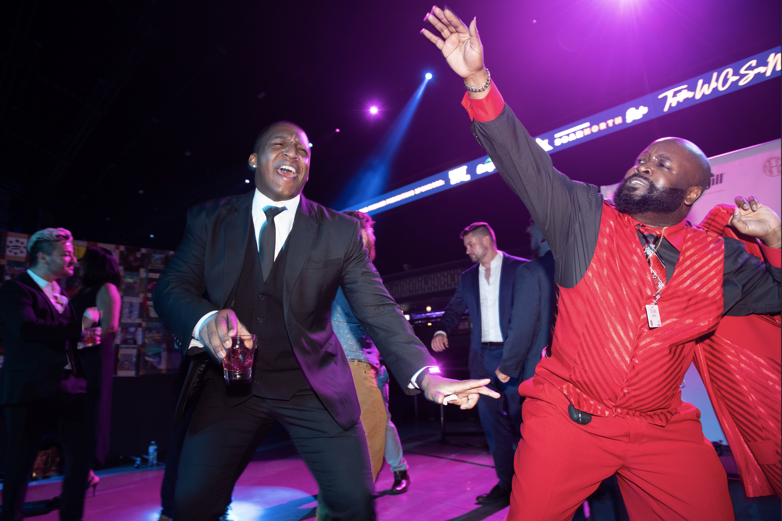 Two men dance at the after party, both are wearing suits and having a good time.