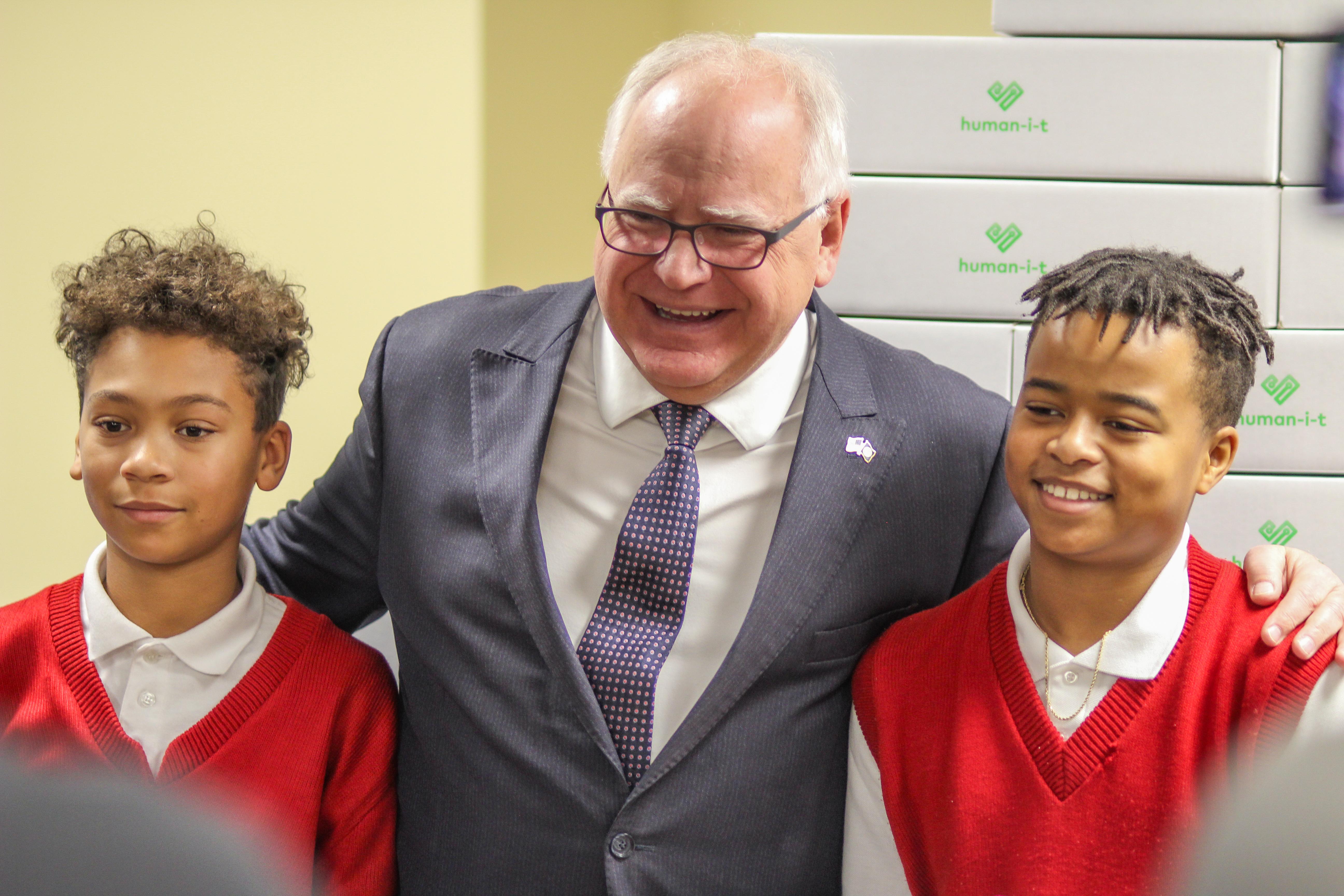 Two young men stand on either side of Minnesota Governor Tim Walz