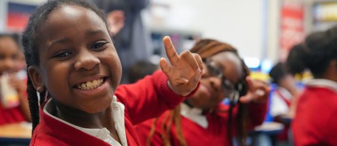 Young girl in uniform smiles at camera while make peace sign