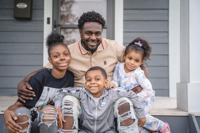 Key and Kids A dad with his three kids sit on the front steps of their home.