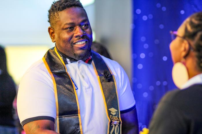 Man smiling wearing stole and shaking a woman's hand.