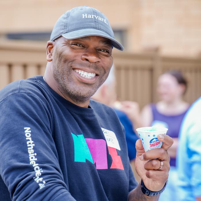 Man smiling, wearing a hat, holding a snow cone